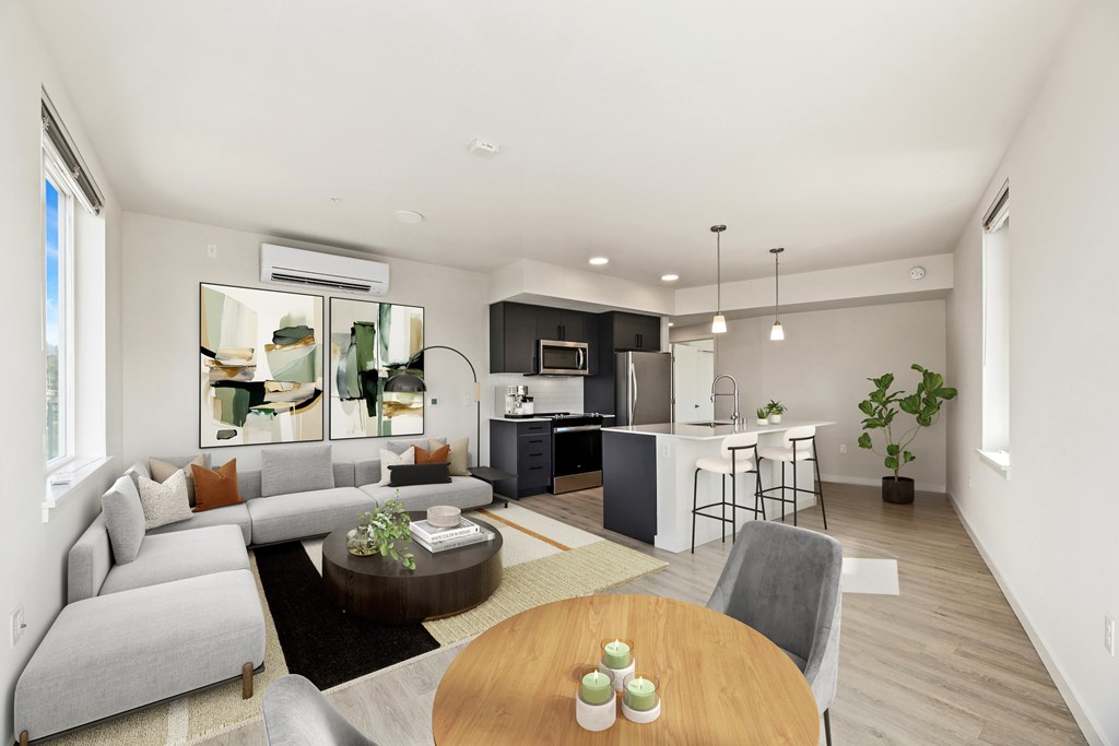 A modern living room with a grey sofa, a wooden coffee table, and a kitchen area in the background.